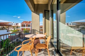 A balcony with a round table and wicker chairs, overlooking a swimming pool and neighboring buildings. - Capital Luxury Suites (Nafplio)