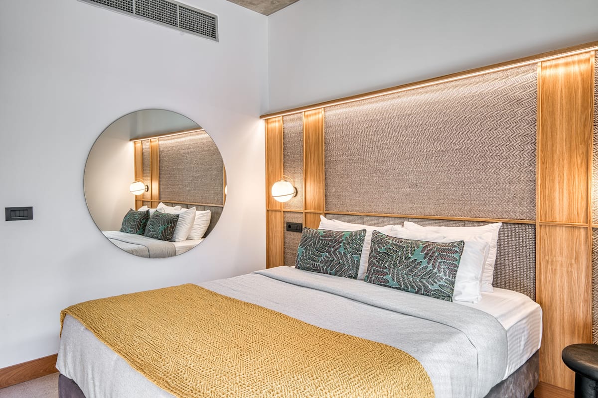 Habitación de hotel con una cama grande, un espejo redondo y un cabecero con panel texturizado.