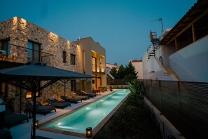 A modern pool area with lounge chairs and a stone building. - Capital Luxury Suites (Nafplio)