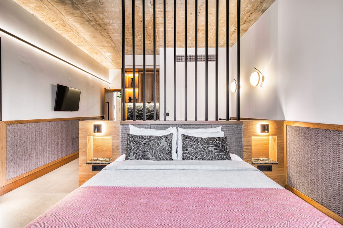 Una habitación de hotel moderna con una cama grande, techo de madera y dos mesitas de noche con lámparas.
