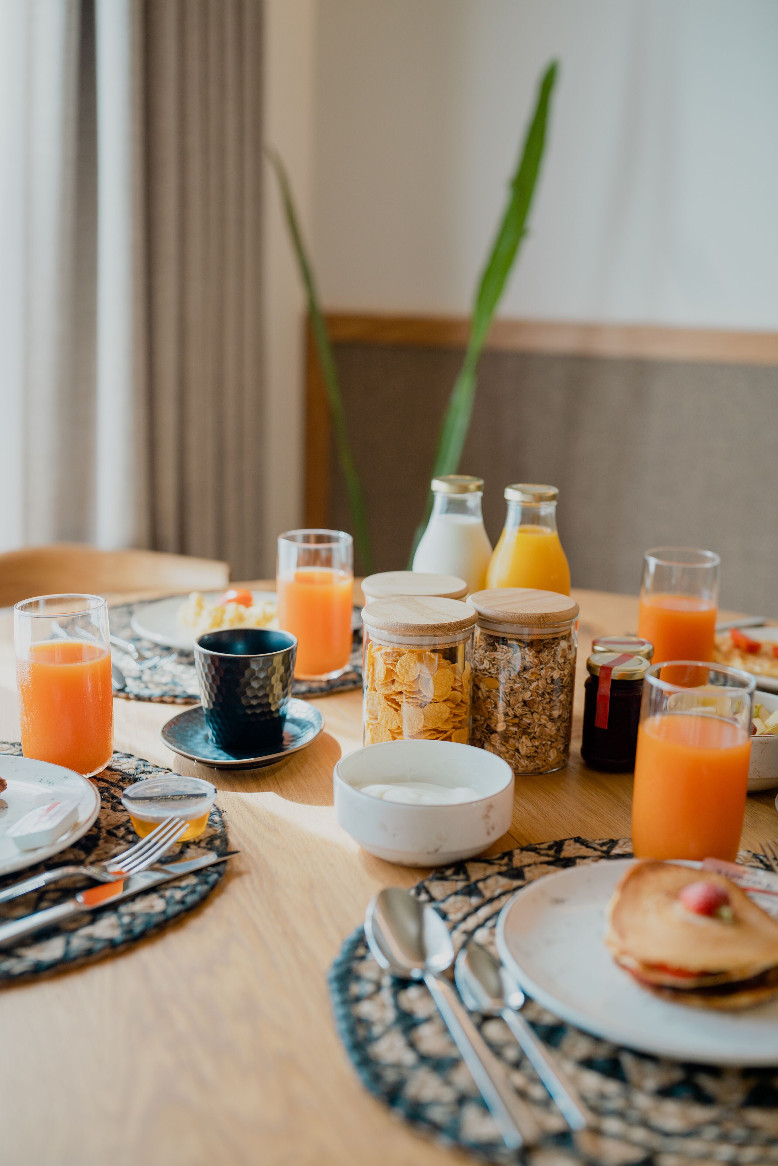 A breakfast table with various food items and drinks, including cereal, pancakes, and orange juice.