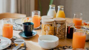 A breakfast table with various food items and drinks, including cereal, pancakes, and orange juice.