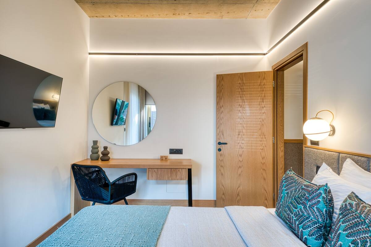 Un dormitorio con cama, escritorio, silla, espejo y puerta.