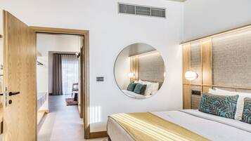 Et moderne hotelværelse med en stor seng, et rundt spejl, et træhovedgærde og en synlig dør, der fører til et andet rum.