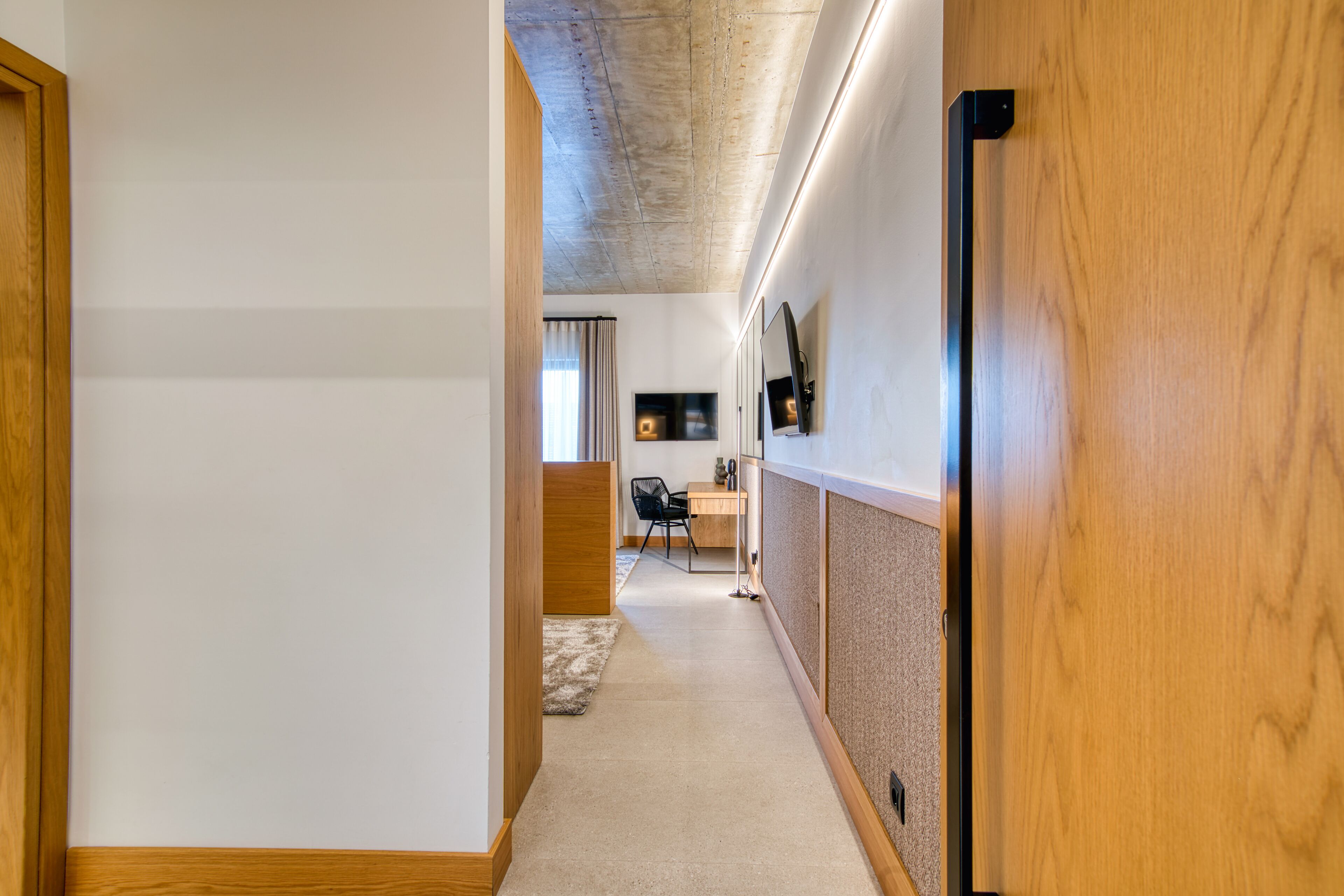 A hallway with a wooden door, a desk with a chair, and a television mounted on the wall.