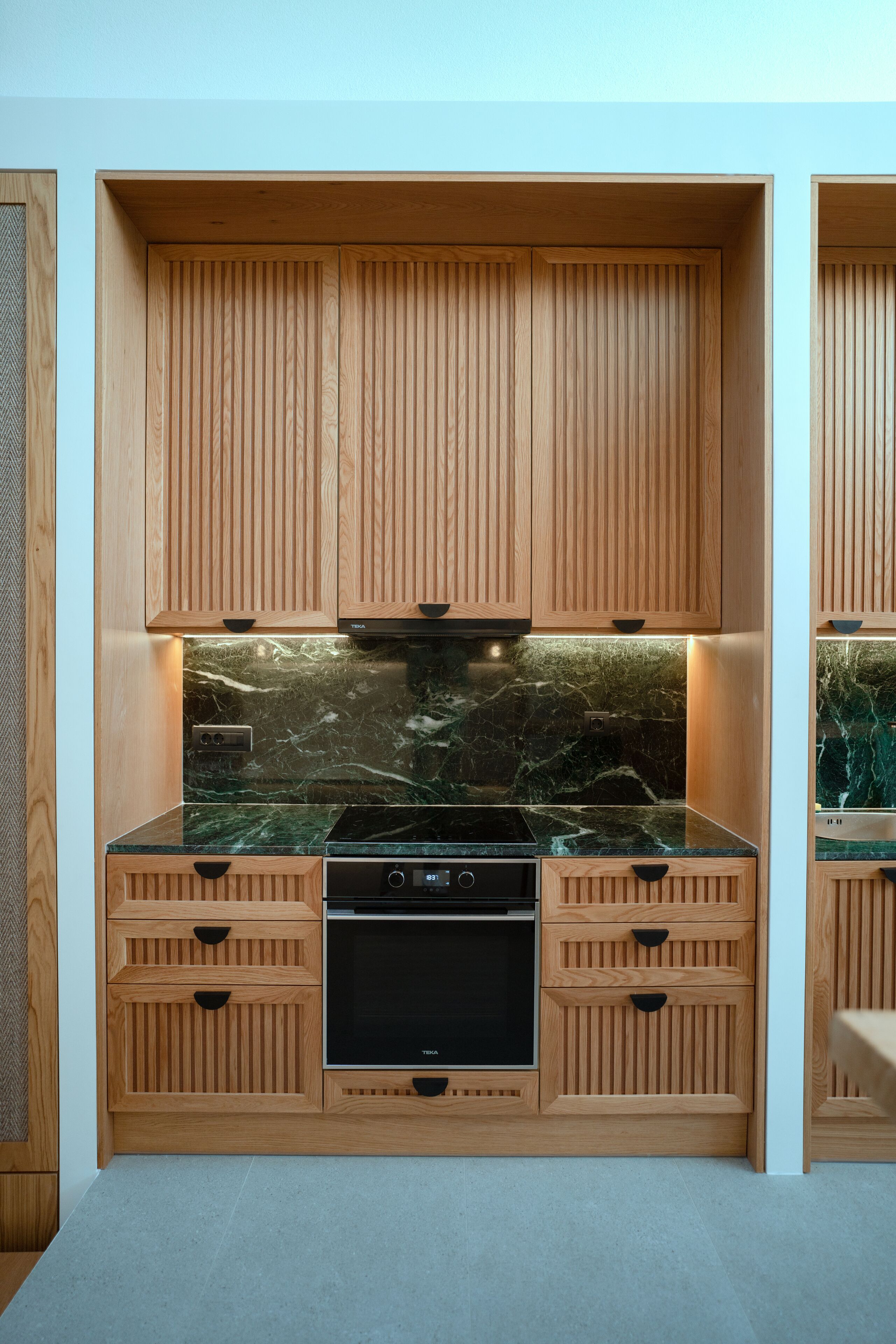 Una cucina moderna con mobili in legno, piano cottura nero e schienale in marmo.