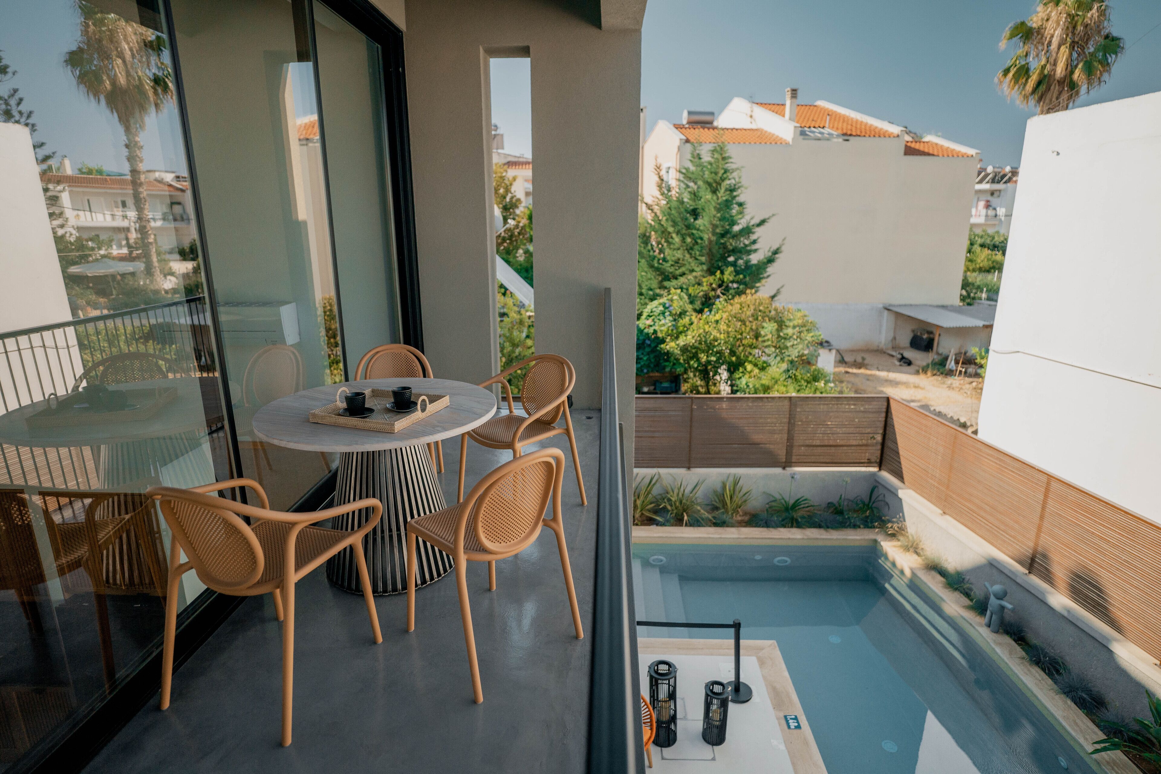 A modern balcony with a round table and wicker chairs, overlooking a swimming pool and a residential area.