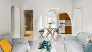 A modern living room with a sofa, a coffee table with decorative items, and an archway leading to a kitchen area. - The Seaview Corner Apartments by Konnect, Ipsos (Corfu)