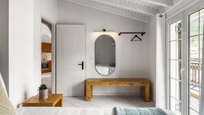 A bedroom with a bed, a wooden bench, a mirror, and a view of a balcony. - The Seaview Corner Apartments by Konnect, Ipsos (Corfu)
