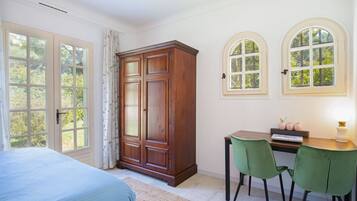 A bedroom with a bed, a wooden wardrobe, a desk with two chairs, and two arched windows.