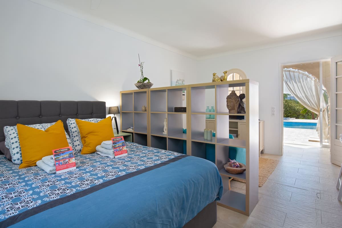 Ein Schlafzimmer mit Bett, Nachttisch, einer Ablage mit Dekoration und Blick ins Freie.