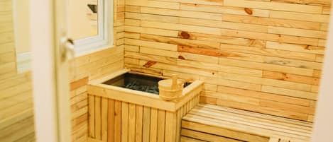 A wooden sauna with a bench and a small wooden container, likely for holding water or towels.