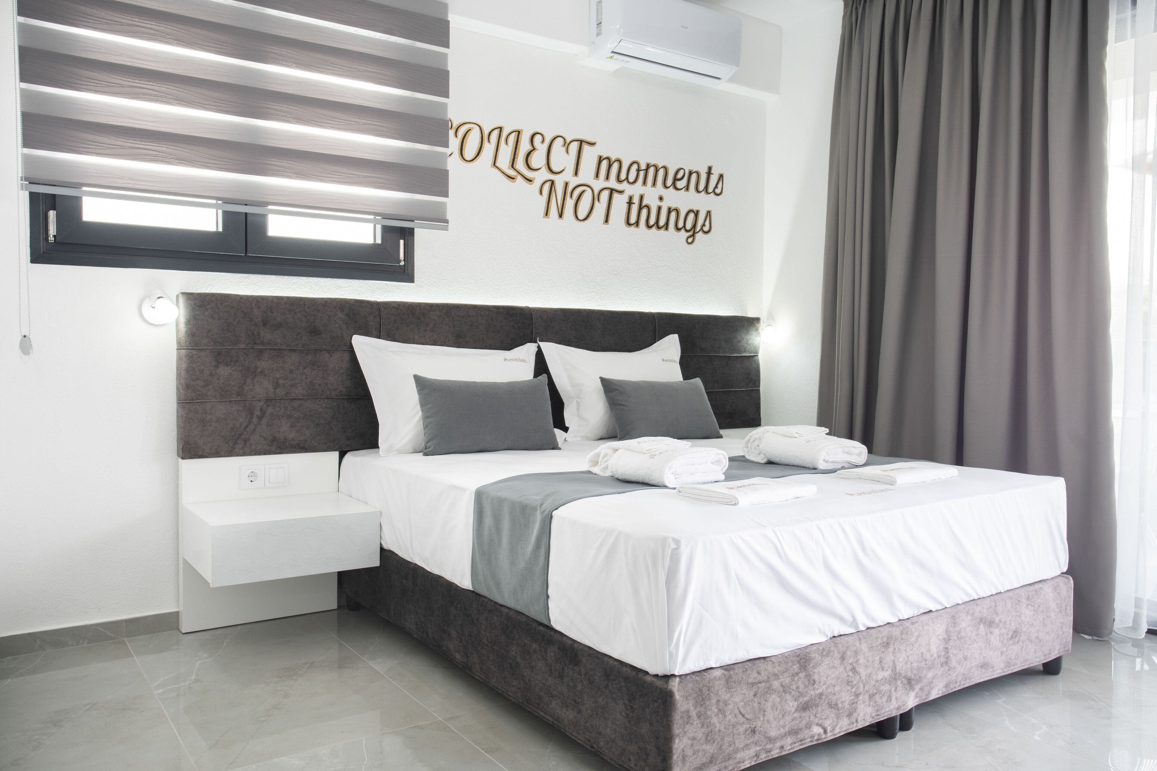 Un dormitorio moderno con cama, mesitas de noche, aire acondicionado instalado en la pared y una frase motivacional.