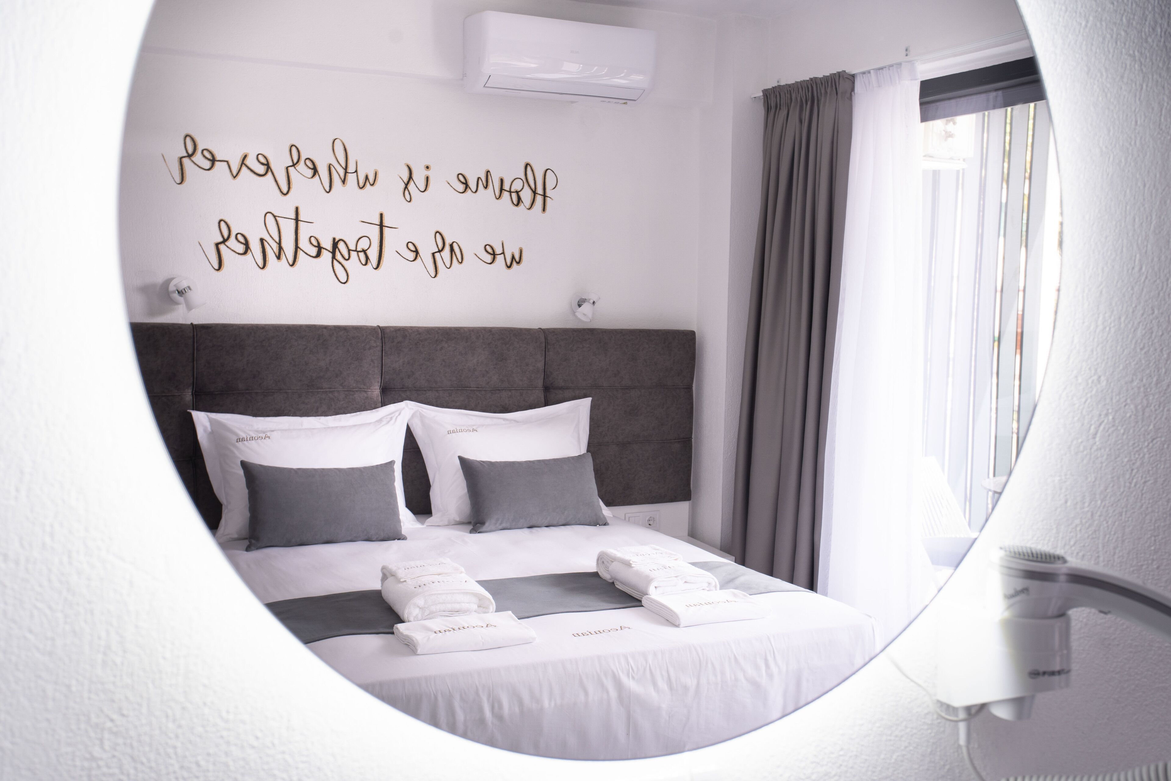 A modern hotel room with a neatly made bed, a wall-mounted air conditioner, and a window with curtains.