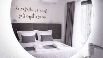 A modern hotel room with a neatly made bed, a wall-mounted air conditioner, and a window with curtains.