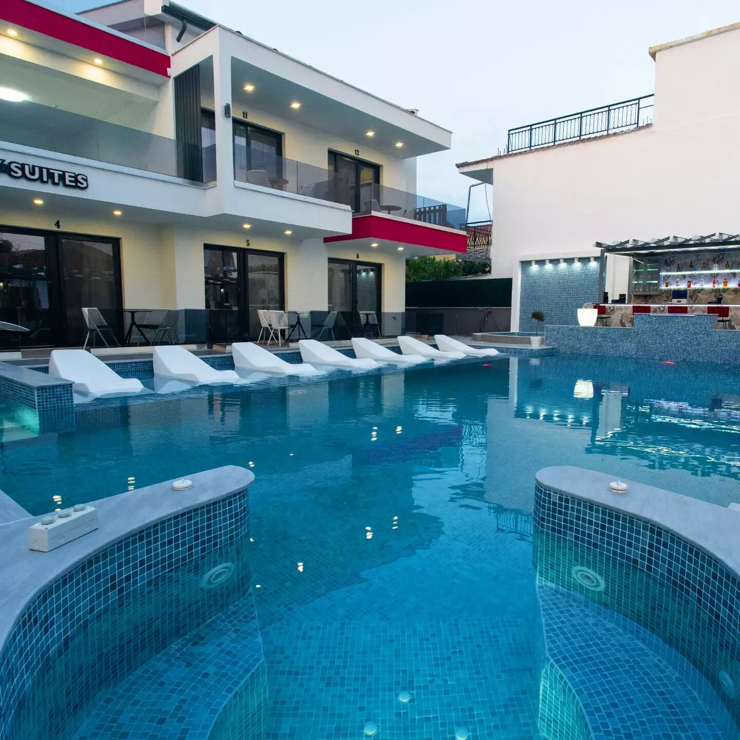 A modern hotel with a pool area, including lounge chairs and a bar.