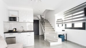 Cocina moderna con microondas integrado, cafetera y lavabo. Se ve una escalera que lleva a una plataforma con un otoman azul.
