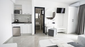 Una habitación de hotel moderna con kitchenette, baño, televisor y cama con almohada decorativa gris.