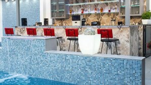 Zona de bar junto a la piscina, con piscina de azulejos, taburetes rojos y un expositor de vidrio con botellas.
