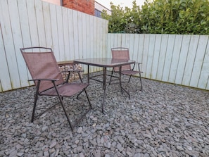 A patio area with a table and two chairs, surrounded by a white fence and a hedge. - 9 North End (Bridlington)