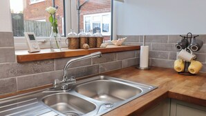 Une cuisine équipée d’un évier à deux bacs, d’une fenêtre donnant sur un immeuble en briques et d’une étagère ornée d’objets décoratifs.