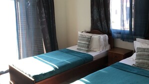 Een kamer met twee eenpersoonsbedden, een plafondventilator, een airconditioning en gordijnen voor de ramen.