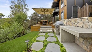 A modern outdoor patio with a stone pathway, a grill, and a wooden deck.