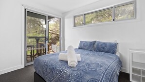 A bedroom with a large bed, a sliding glass door leading to an outdoor area, and a window with a view of trees.
