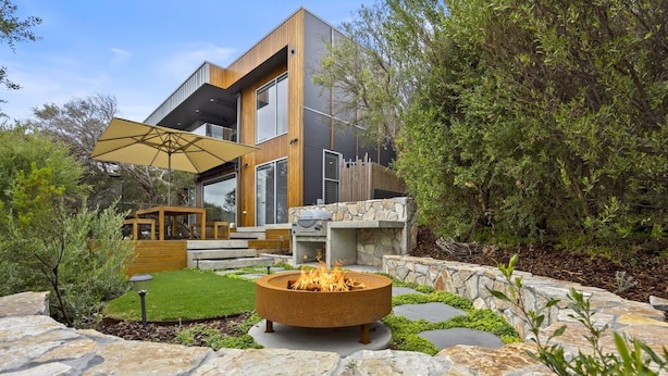 A modern house with a stone fire pit, a wooden deck, and a stone wall.