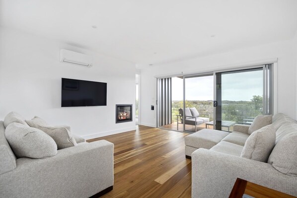 A modern living room with a fireplace, a flat-screen TV, and a large sliding glass door leading to an outdoor patio. - Sunset on Moonah. (Fingal)