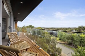 A balcony with wooden chairs and a potted plant, overlooking a road and greenery. - Sunset on Moonah. (Fingal)
