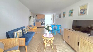Een woonkamer met een bank, stoelen, een televisie en een keuken op de achtergrond.