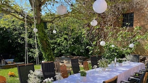 An outdoor dining area with a long table set for multiple guests, surrounded by chairs and decorated with white flowers and candles. - Nußriegel vacation apartment in a historic setting on the wine route (Bad Dürkheim)