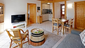 A cozy living room with a television, wooden furniture, a dining area, and a kitchen. - Nußriegel vacation apartment in a historic setting on the wine route (Bad Dürkheim)
