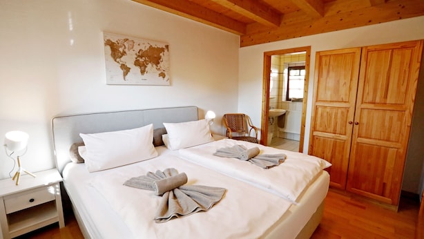 A double bed with white linens and towels, a bedside table with a lamp, a wooden wardrobe, and a world map on the wall. - Nußriegel vacation apartment in a historic setting on the wine route (Bad Dürkheim)