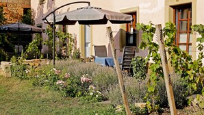 A garden with a table and chairs, a pergola with an umbrella, and a building with a window and door. - Nußriegel vacation apartment in a historic setting on the wine route (Bad Dürkheim)