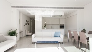 A modern living room with a white sofa, a coffee table, and a dining area with chairs and a table. - Athens Observatory Suite - Breathtaking views of the Acropolis (Athina)