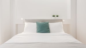 A neatly made bed with white linens and a teal pillow, a small potted plant on the nightstand, and a minimalist wall design. - Athens Observatory Suite - Breathtaking views of the Acropolis (Athina)