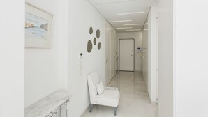 A modern, clean hallway with a white chair, a framed picture, and a door at the end. - Athens Observatory Suite - Breathtaking views of the Acropolis (Athina)