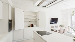 A modern kitchen with white cabinetry, a built-in oven, and a dining area with a table and chairs. - Athens Observatory Suite - Breathtaking views of the Acropolis (Athina)