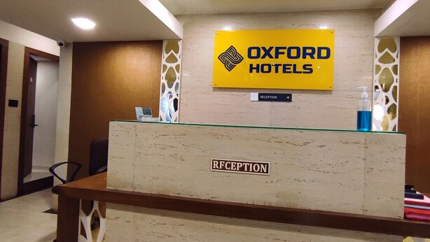 A reception desk with a sign for Oxford Hotels, a reception label, and a directional sign to the reception. - Oxford Hotel Powai (Mumbai)