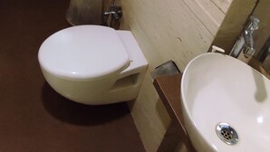 A bathroom with a toilet, sink, and a towel hanging on the wall. - Oxford Hotel Powai (Mumbai)
