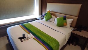 A hotel room with a bed, pillows, a bedside table, and a window. - Oxford Hotel Powai (Mumbai)