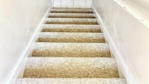 Una escalera con peldaños alfombrados que conduce a un rellano con un tapete estampado.