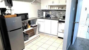 Una cocina compacta con gabinetes blancos, un refrigerador, un microondas y un lavamanos.