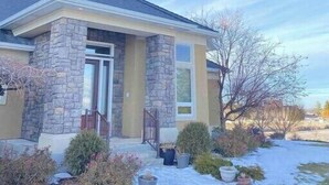 Una casa de una sola planta con fachada de piedra, puerta principal y un pequeño porche con plantas en macetas.