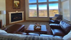 Una sala de estar con chimenea, ventanas amplias con vistas, y mobiliario de cuero.