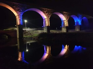 A stone bridge with arches at night, illuminated by blue and purple lights, reflecting on the water below. - Zen Cottage, Cullen - Sleeps 4, Garden & Pets Ok (Buckie)