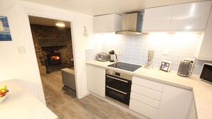 A modern kitchen with white cabinets, a built-in oven, a stove, and a stone fireplace. - Zen Cottage, Cullen - Sleeps 4, Garden & Pets Ok (Buckie)