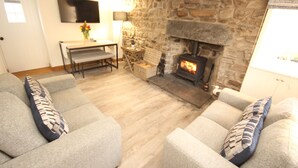 A cozy living room with a stone fireplace, grey sofas, and a flat-screen TV mounted on the wall. - Zen Cottage, Cullen - Sleeps 4, Garden & Pets Ok (Buckie)